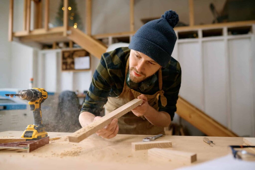 Young carpenter man blowing saw dust in workshop